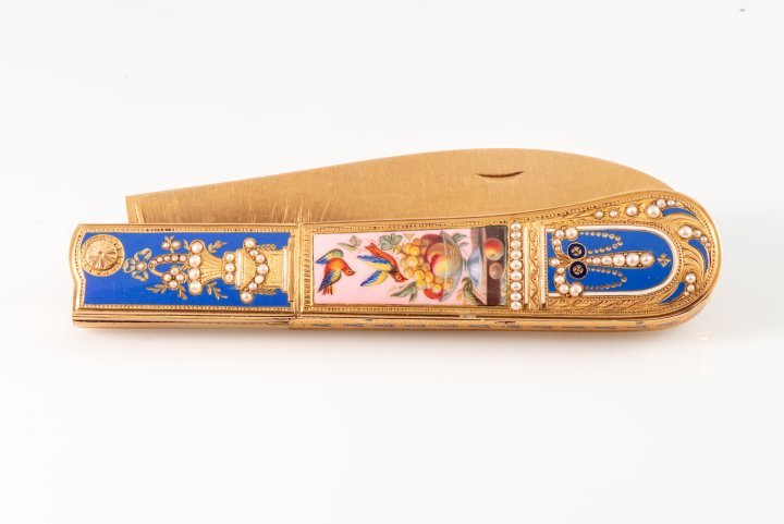 One of the most exceptional shape timepieces in this auction is LOT 457, an outstanding double- bladed pocket-knife with a watch and music. This knife was made for the Chinese market circa 1805- 1815 and is crafted from 18K yellow gold, enamel, and pearls and features a white enamel dial with suspended “Breguet” numerals. The tapered mount is decorated with fine cut engravings and sky blue champlevé enamel with floral motifs and urns set with half-pearls. The back panel boasts a polychrome enamel plaque on a pink background with fruit and birds. The knife's two folding blades are made of steel and gold, and the watch is a key-winding fantasy watch.