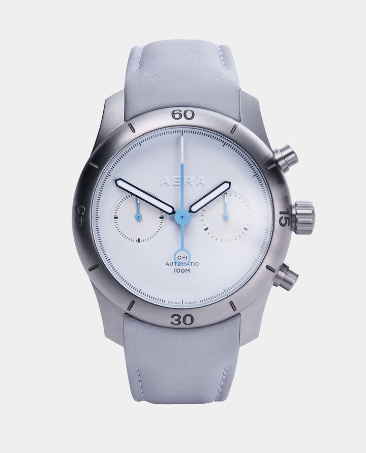 The chronograph seconds hand and sub dial hands are in a sky blue lacquer. The grey framed hour and minute sword hands are hand-filled with white Grade X1 Swiss Super-LumiNova. The chronograph seconds hand and pointers have crisp white Grade X1 Swiss Super-LumiNova tips, which glow green for night time clarity. The Aera logo, which is cut from solid white GlobolightTM, glows white in contrast to the strong green of the hands.