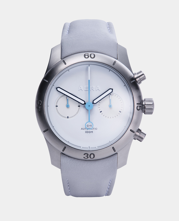The chronograph seconds hand and sub dial hands are in a sky blue lacquer. The grey framed hour and minute sword hands are hand-filled with white Grade X1 Swiss Super-LumiNova. The chronograph seconds hand and pointers have crisp white Grade X1 Swiss Super-LumiNova tips, which glow green for night time clarity. The Aera logo, which is cut from solid white GlobolightTM, glows white in contrast to the strong green of the hands.
